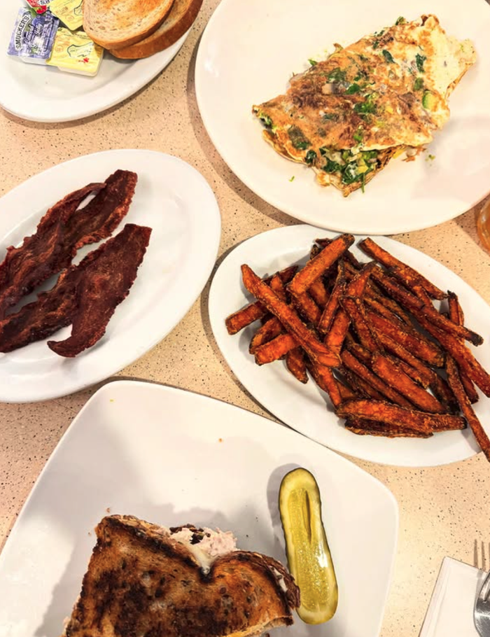Table spread with omelette, bacon, sweet potato fries, toast, and a sandwich.