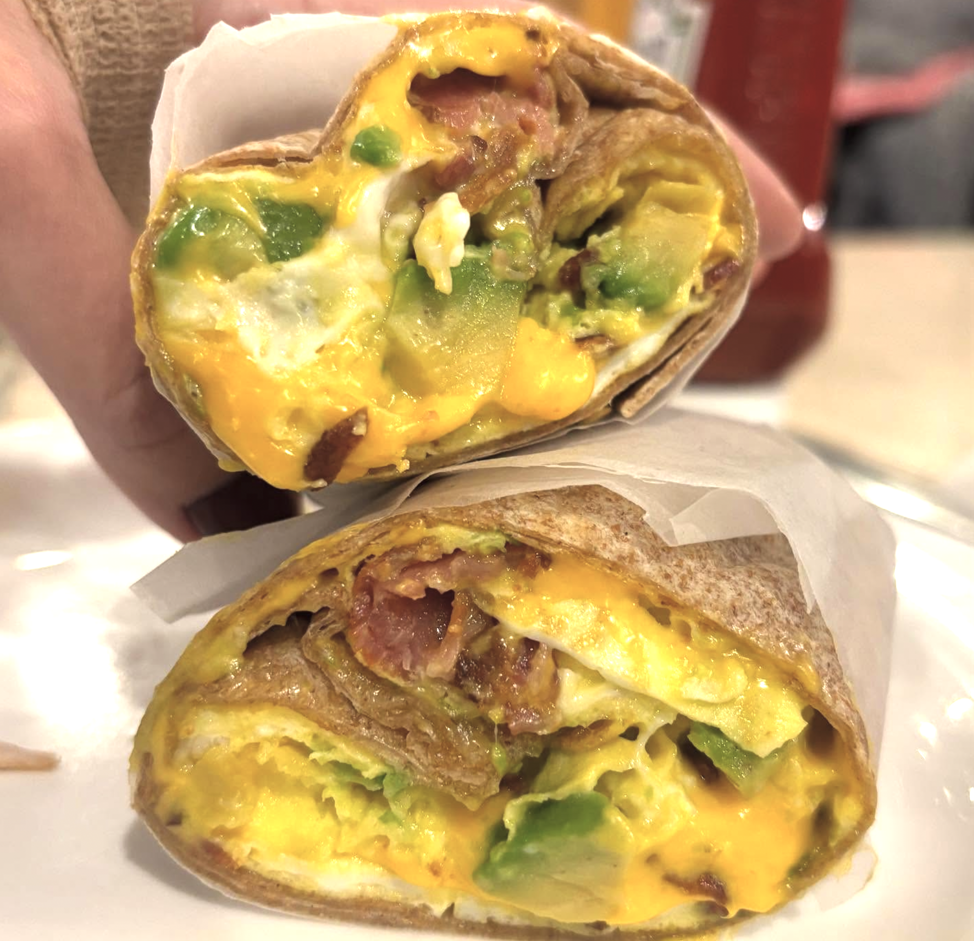 Breakfast wrap with egg, avocado, bacon, and melted cheese.