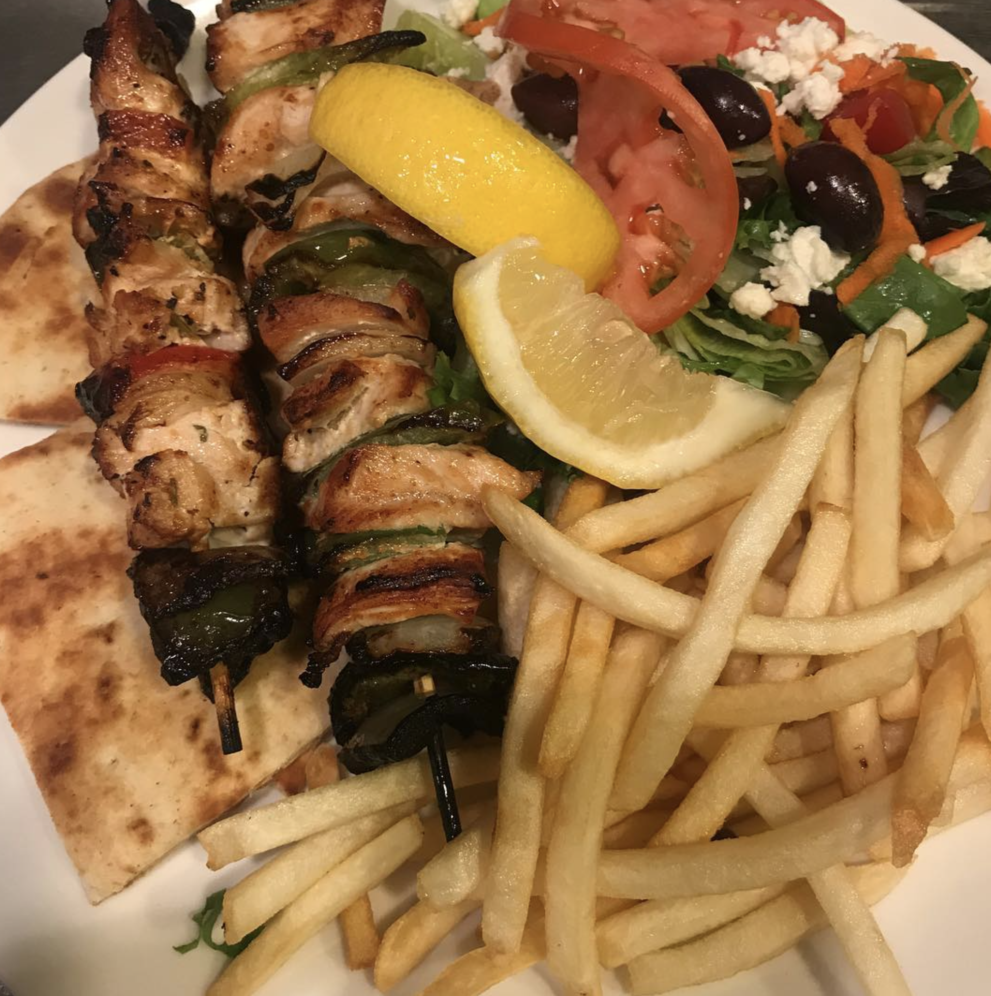 Chicken souvlaki skewers with Greek salad, pita, fries, and lemon.