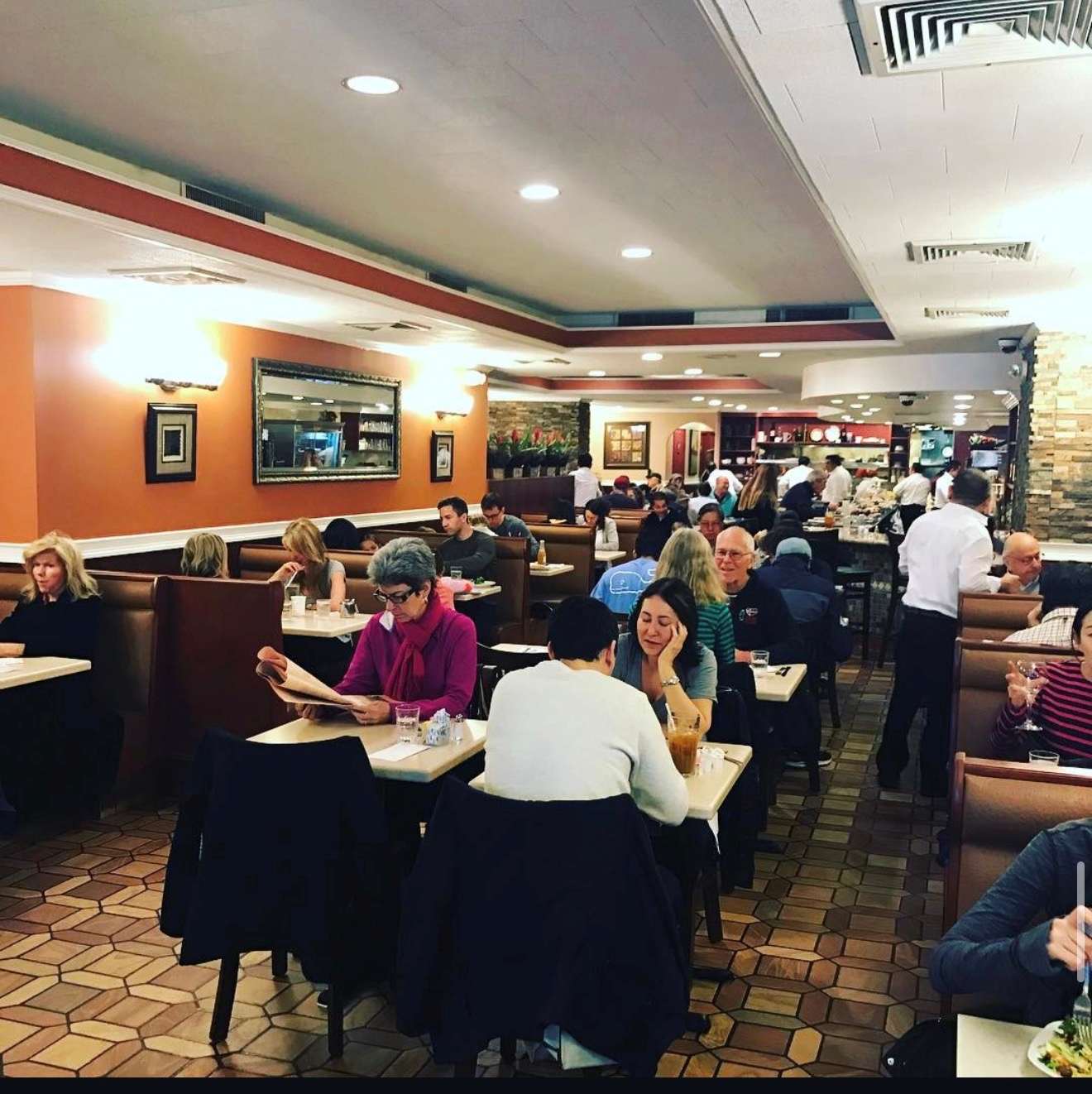 Three Guys dining room full during service with booths, orange walls, and staff at work.